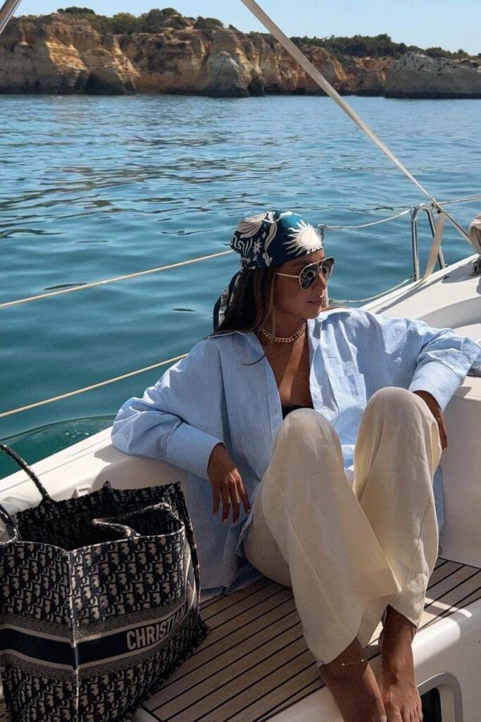 19 Chicest Beach Outfits That Belong in Your Summer Photo Dump pinstripe yacht shirt, cream trousers, and silk headscarf